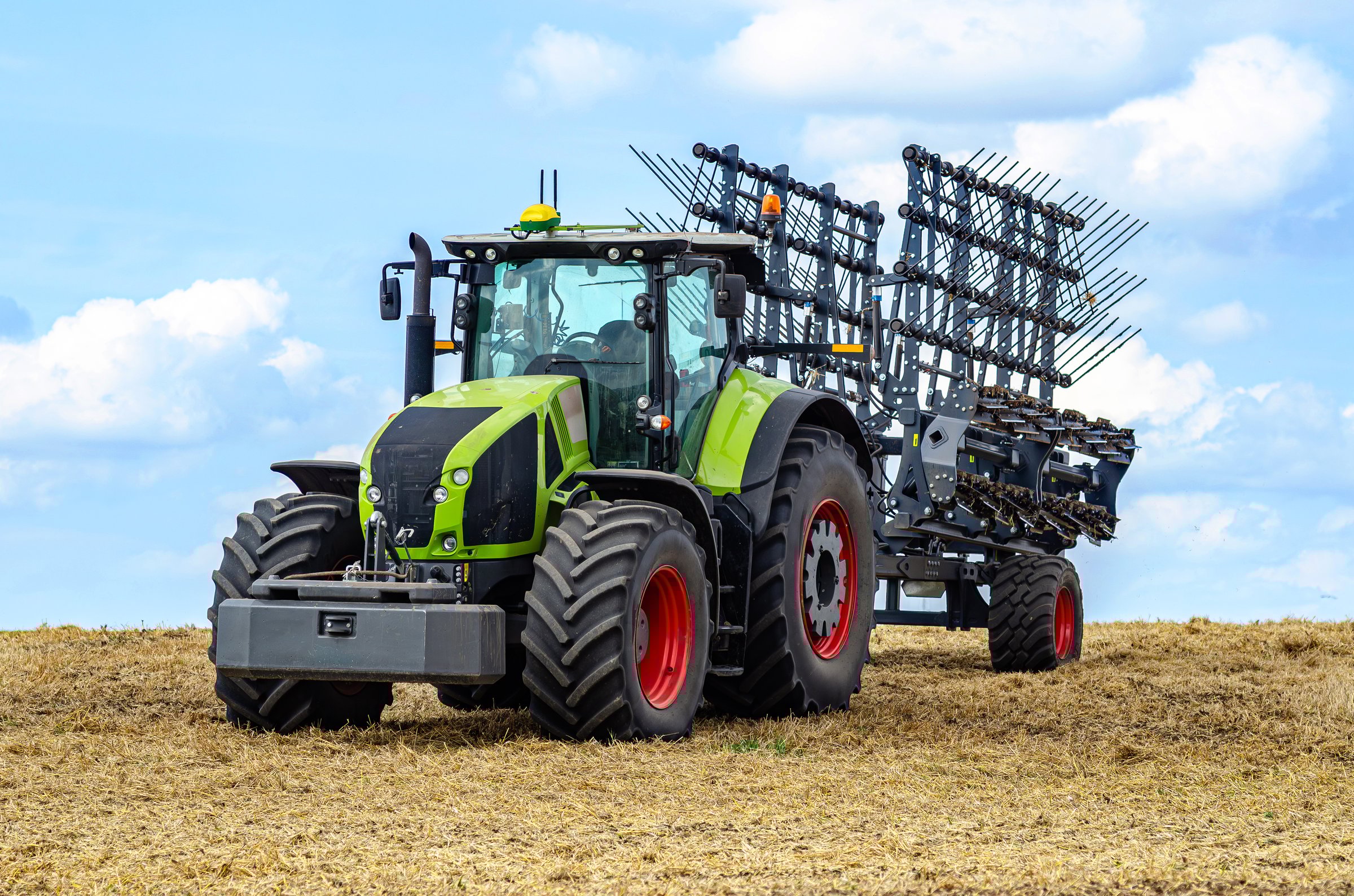 Modern tractor on stubble in field under cloudy sky. Concept of work in fields and agricultural industry. Soil cultivator. Side view.