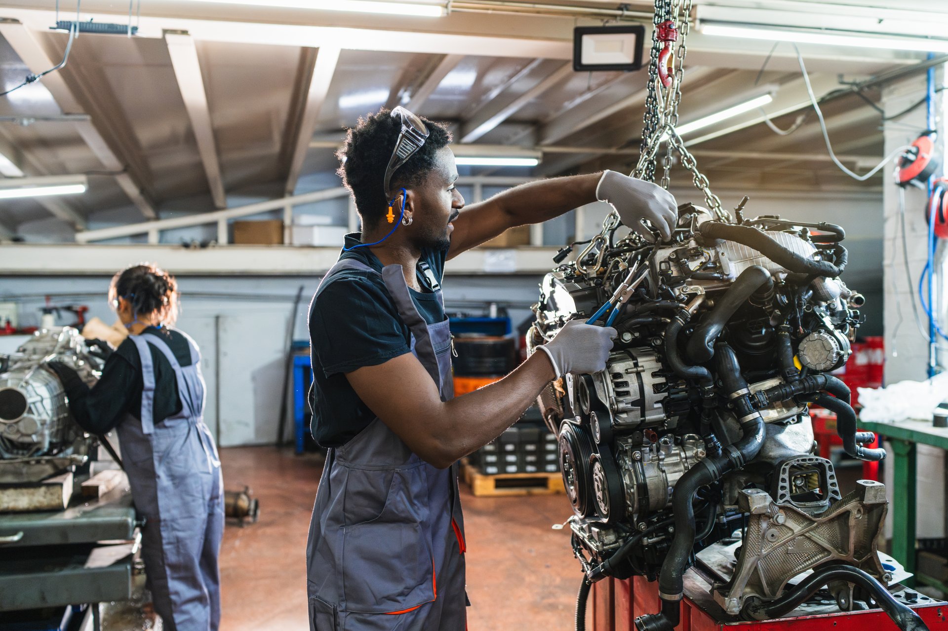 Two auto mechanics working on a car engine using specialized tools in a professional car repair shop environment